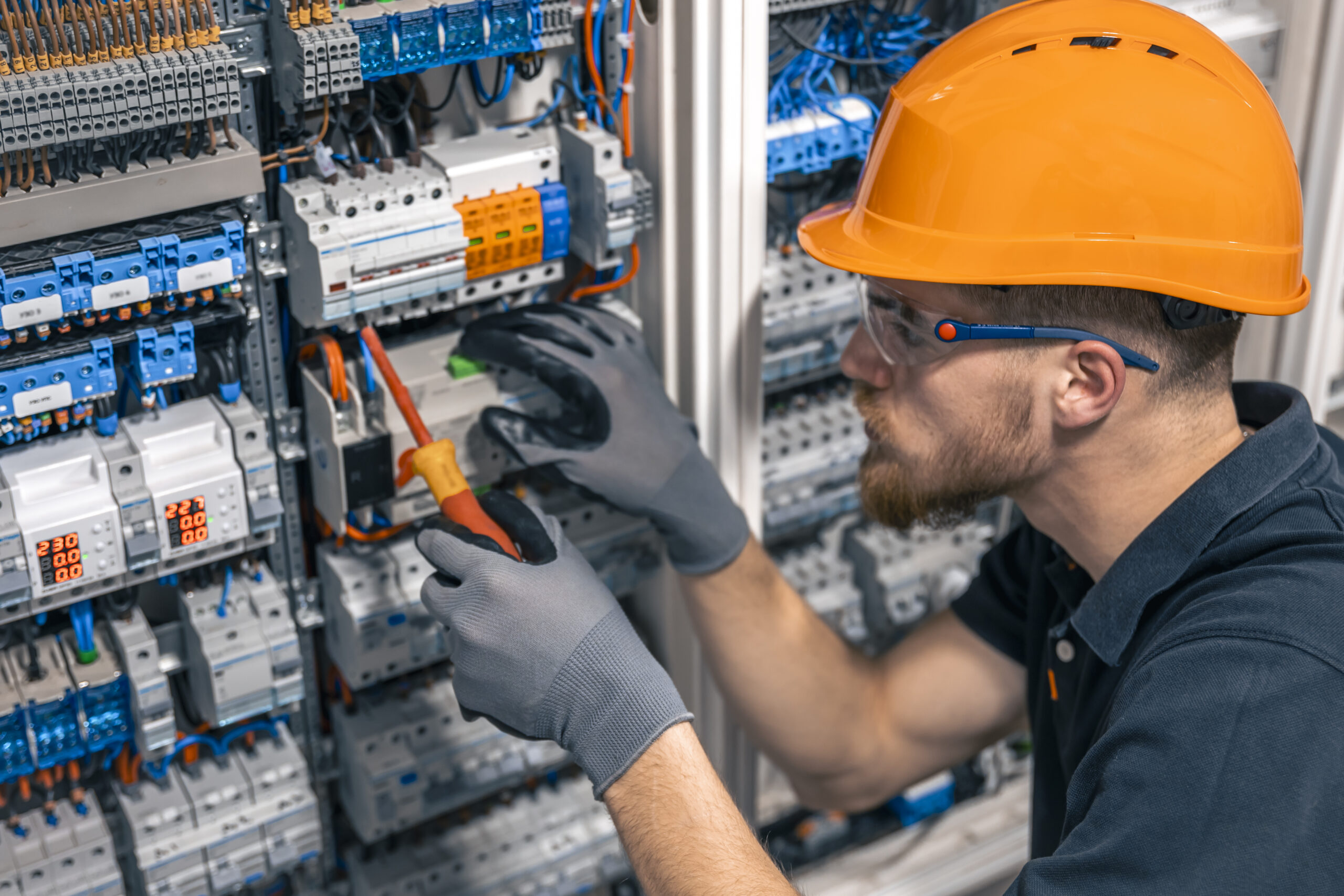 Male electrician working in a switchboard with fuses. Installation and connection of electrical equipment. Professional with tools in hand.